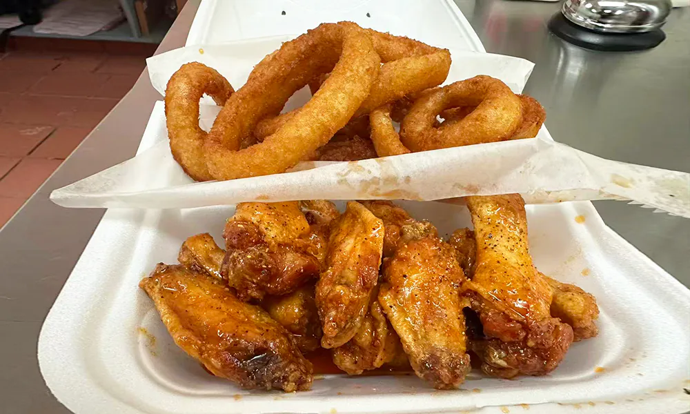 Buffalo sauce-coated chicken wings paired with crispy onion rings at Kick Off Wings, a Fast Food Restaurant in Carrollton